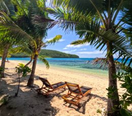 A serene tropical island beach is set with brown deck chairs inviting sunbakers to lounge in the sun